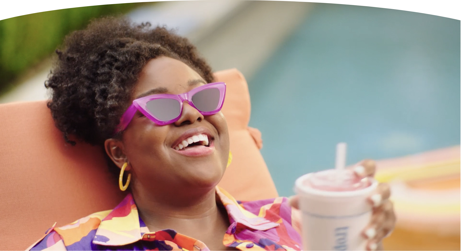 Tropical Smoothie Cafe Rewards member enjoying a Free Tropical Smoothie by the pool wearing purple sunglasses.
